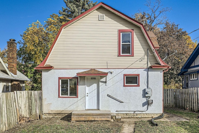view of front of home with a gambrel roof, stucco siding, and fence