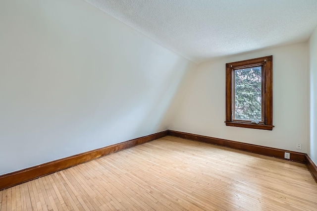 additional living space featuring baseboards, light wood-type flooring, and a textured ceiling