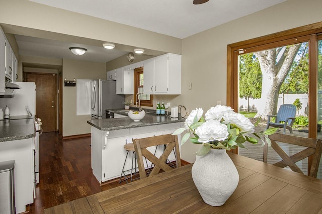 kitchen with a peninsula, white cabinetry, a sink, dark wood-style flooring, and dark countertops
