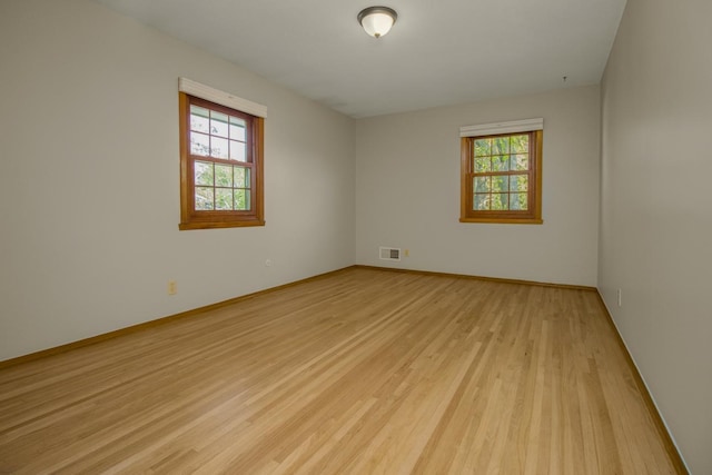 spare room featuring plenty of natural light, light wood finished floors, and baseboards