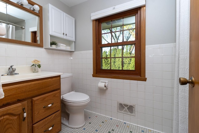 bathroom with tile walls, tile patterned floors, toilet, vanity, and a wainscoted wall