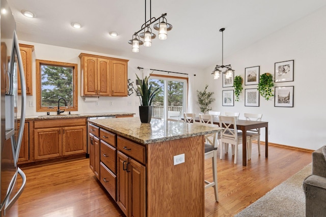 kitchen featuring a sink, vaulted ceiling, stainless steel fridge, a kitchen breakfast bar, and light stone countertops