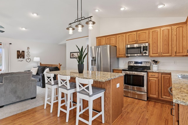 kitchen featuring appliances with stainless steel finishes, open floor plan, a center island, light wood finished floors, and light stone counters