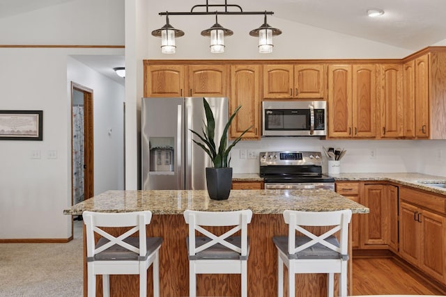 kitchen featuring appliances with stainless steel finishes, lofted ceiling, light stone countertops, a breakfast bar, and pendant lighting