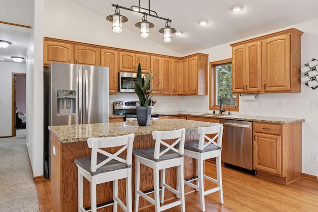 kitchen featuring stainless steel appliances, lofted ceiling, a sink, a kitchen island, and light stone countertops