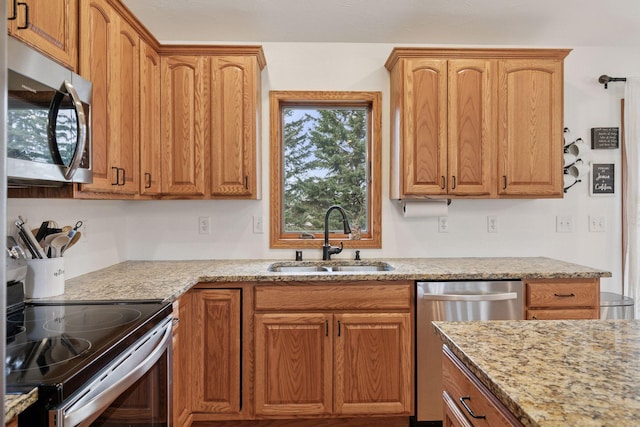 kitchen featuring stainless steel appliances, a sink, light stone counters, and brown cabinetry