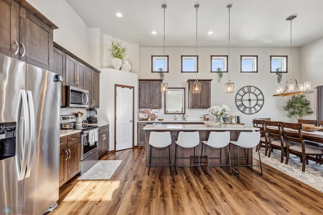 kitchen with a kitchen bar, dark brown cabinets, appliances with stainless steel finishes, wood finished floors, and decorative backsplash