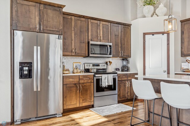 kitchen with light wood-style floors, appliances with stainless steel finishes, decorative backsplash, and light countertops