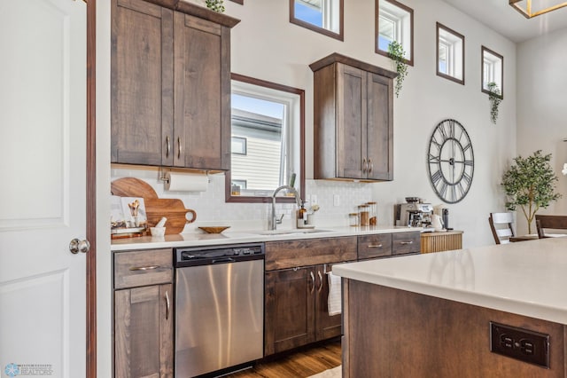 kitchen with light countertops, dark wood-type flooring, decorative backsplash, dishwasher, and a sink