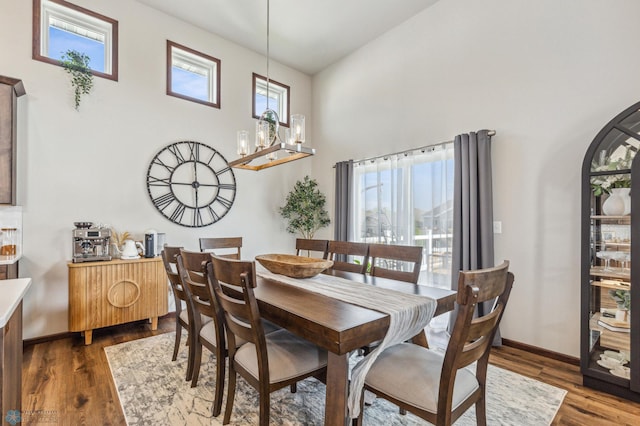 dining room featuring dark wood-type flooring, baseboards, an inviting chandelier, and a towering ceiling