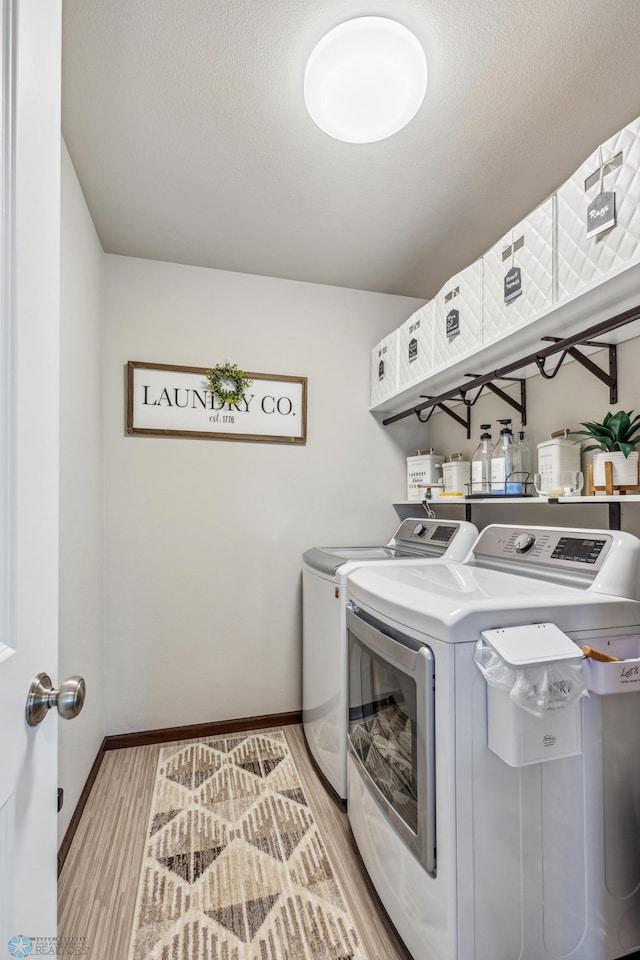 clothes washing area with baseboards, a textured ceiling, light wood-style floors, laundry area, and washing machine and clothes dryer