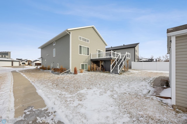 snow covered rear of property featuring fence, a deck, and stairs