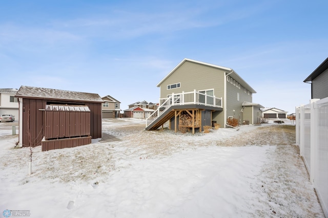 snow covered back of property featuring a shed, stairway, a wooden deck, and an outbuilding