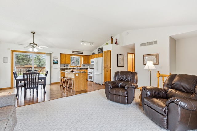 living room with visible vents, wood finished floors, a ceiling fan, and lofted ceiling