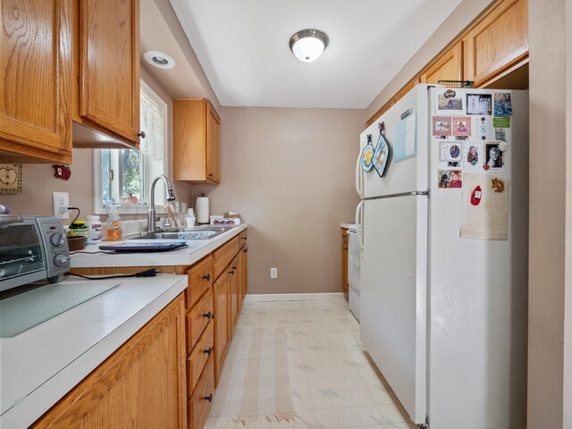 kitchen with baseboards, light countertops, freestanding refrigerator, light floors, and a sink