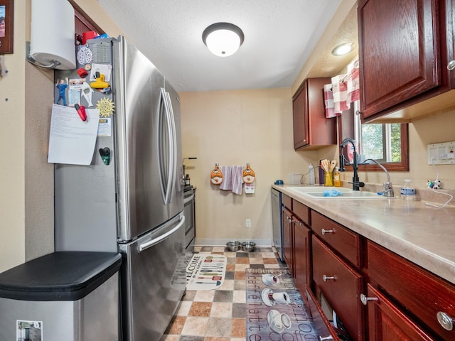 kitchen with baseboards, a sink, light countertops, stainless steel appliances, and light floors