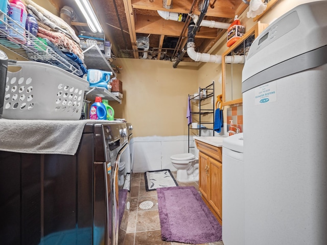 bathroom with stone finish flooring, wainscoting, independent washer and dryer, and toilet