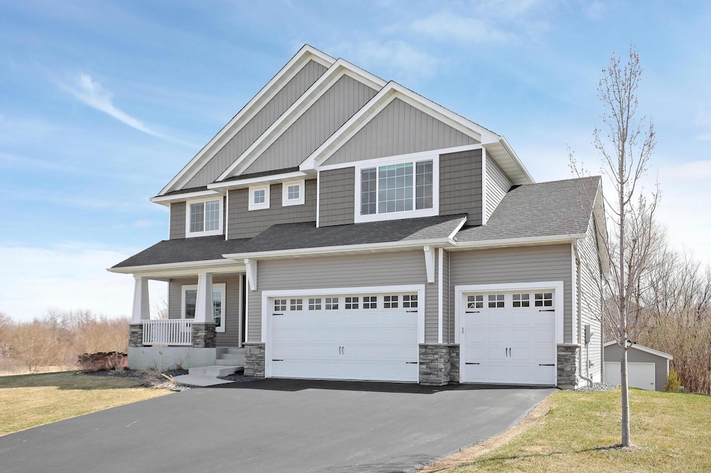 craftsman-style house with a front lawn, stone siding, covered porch, a garage, and aphalt driveway