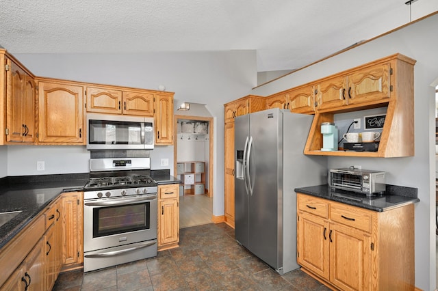 kitchen featuring lofted ceiling, a toaster, stone finish floor, a textured ceiling, and stainless steel appliances