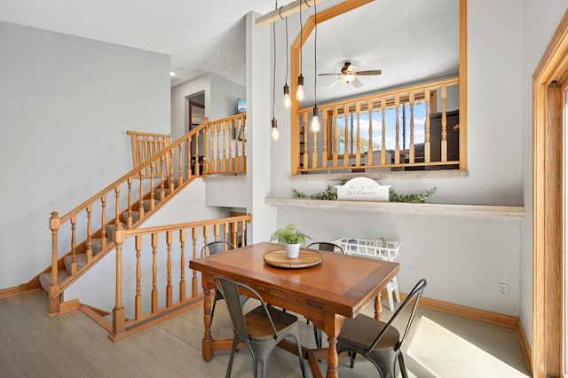 dining space featuring a ceiling fan, baseboards, wood finished floors, and stairway