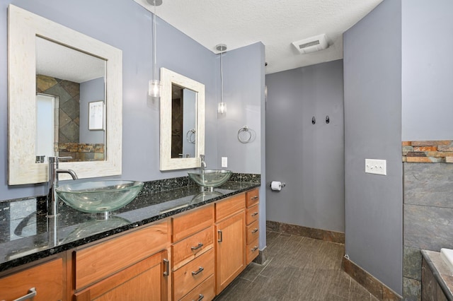 full bathroom with baseboards, double vanity, a textured ceiling, and a sink