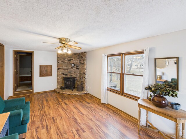 living room with a wood stove, ceiling fan, a textured ceiling, and wood finished floors