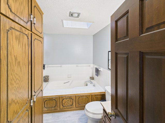 full bathroom with a garden tub, a textured ceiling, a wainscoted wall, toilet, and a skylight