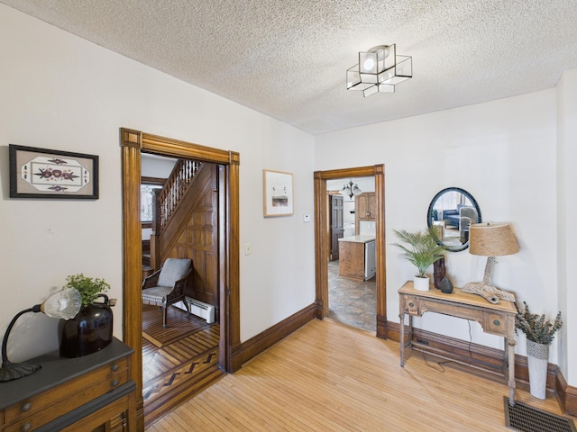 hallway featuring light wood-style flooring, baseboards, and a textured ceiling