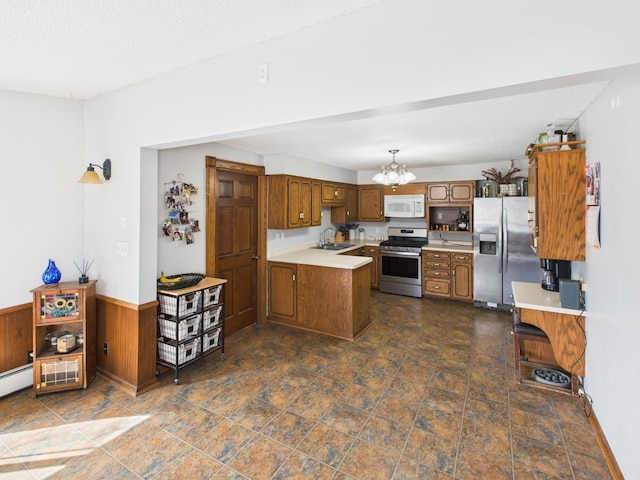 kitchen featuring an inviting chandelier, brown cabinetry, a peninsula, a sink, and stainless steel appliances