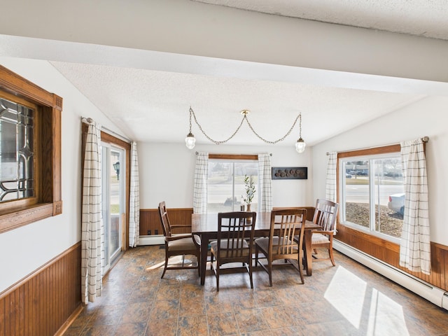 dining area featuring wood walls, plenty of natural light, baseboard heating, and wainscoting