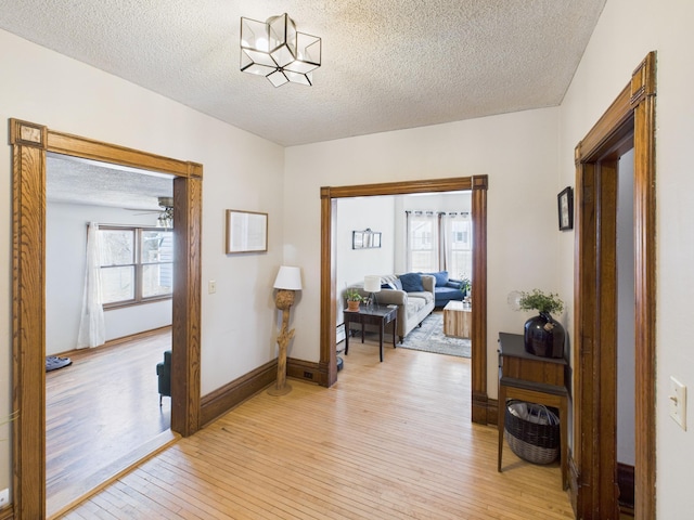 corridor featuring light wood-style floors, a textured ceiling, and baseboards