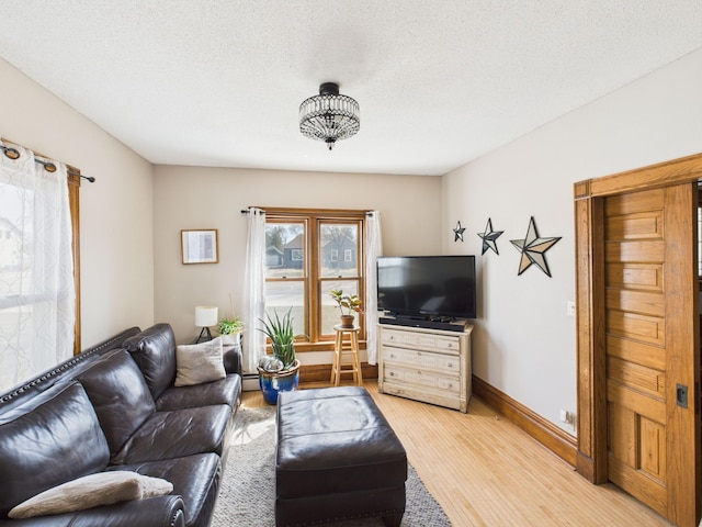 living area featuring light wood-type flooring, baseboards, and a textured ceiling