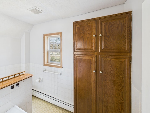 bathroom featuring a wainscoted wall, tile walls, a baseboard radiator, and visible vents
