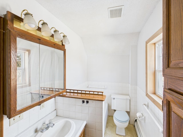 bathroom with toilet, visible vents, wainscoting, tile walls, and a sink
