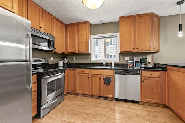 6491 Regency Ln, Eden Prairie, MN 55344 - kitchen with appliances with stainless steel finishes, dark countertops, brown cabinetry, light wood finished floors, and a textured ceiling
