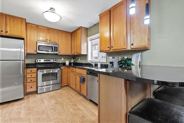 6491 Regency Ln, Eden Prairie, MN 55344 - kitchen with appliances with stainless steel finishes, brown cabinets, light wood finished floors, a breakfast bar area, and a textured ceiling