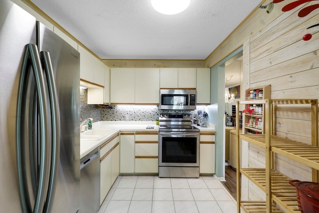 kitchen featuring appliances with stainless steel finishes, a sink, light countertops, a textured ceiling, and backsplash