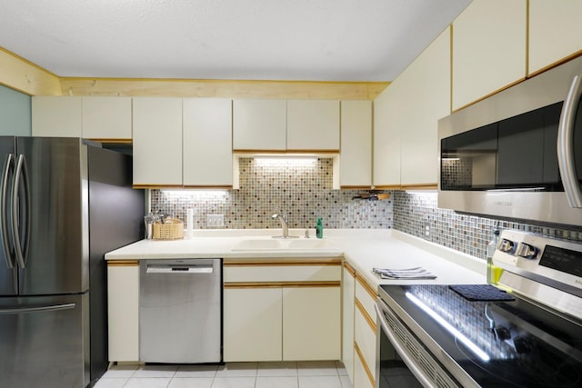 kitchen featuring appliances with stainless steel finishes, a sink, cream cabinets, light countertops, and tasteful backsplash