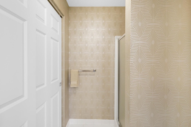 bathroom with wallpapered walls and a shower with shower door