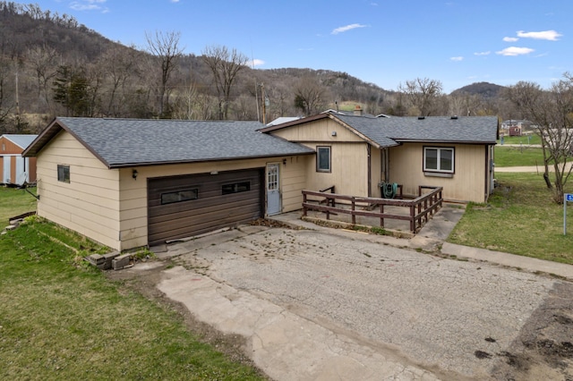 ranch-style house featuring a shingled roof, an attached garage, driveway, a front yard, and a mountain view