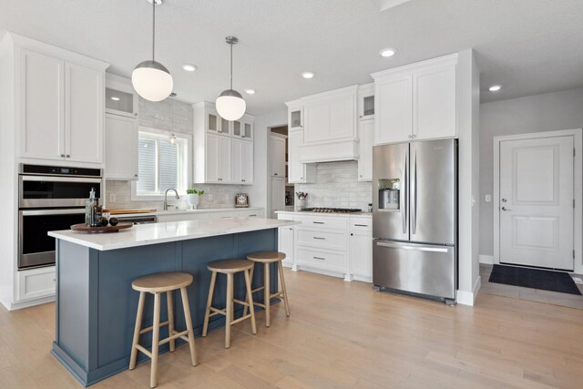 kitchen with tasteful backsplash, stainless steel appliances, light wood finished floors, a kitchen bar, and a sink