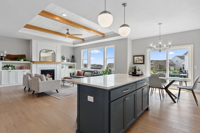 kitchen featuring a tiled fireplace, a tray ceiling, a center island, light wood-type flooring, and pendant lighting