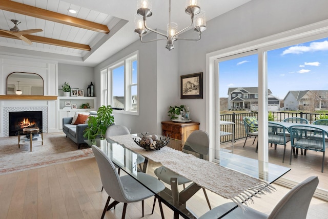 dining area featuring a tile fireplace, a residential view, a raised ceiling, light wood-style flooring, and ceiling fan with notable chandelier