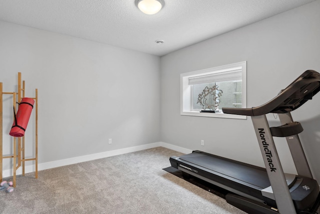 workout area featuring baseboards, a textured ceiling, and carpet