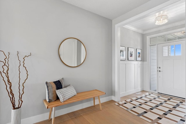 entrance foyer featuring light wood-style floors, a notable chandelier, baseboards, ornamental molding, and wainscoting