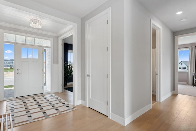 foyer with an inviting chandelier, wainscoting, light wood finished floors, baseboards, and crown molding