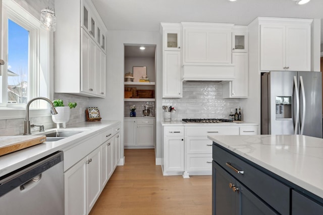 kitchen with white cabinetry, tasteful backsplash, a sink, light wood-style floors, and stainless steel appliances