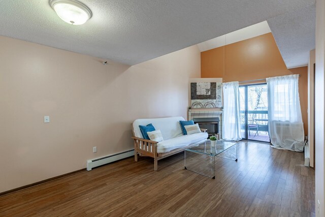 living area with a tile fireplace, wood finished floors, baseboards, a baseboard radiator, and a textured ceiling