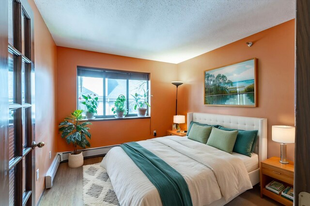 bedroom featuring a baseboard radiator, wood finished floors, a textured ceiling, and baseboards