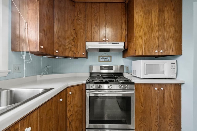 kitchen with stainless steel gas range, brown cabinets, under cabinet range hood, white microwave, and light countertops